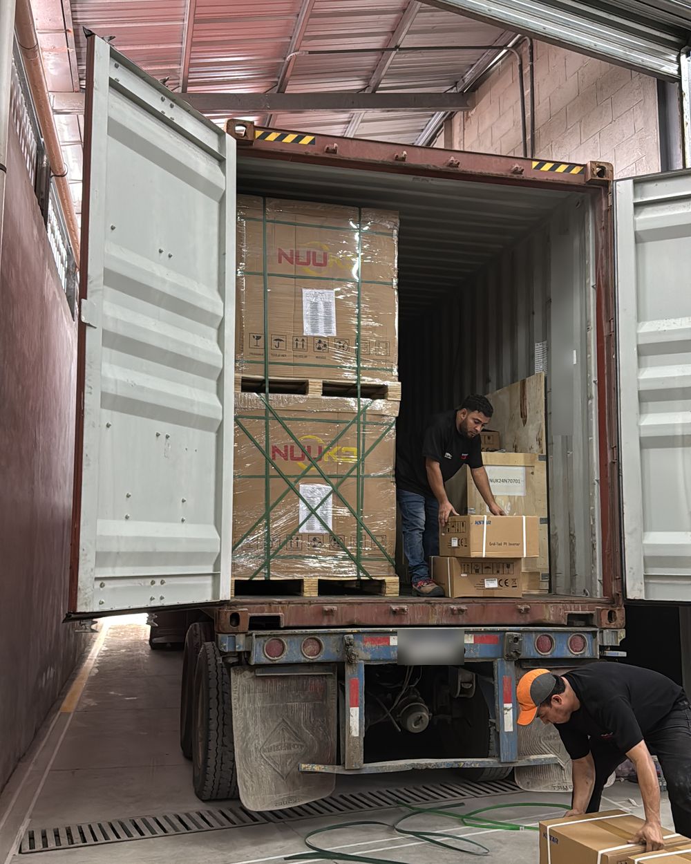 Contenedor abierto con pallets de módulos solares Nuuko y cajas de inversores, durante la descarga